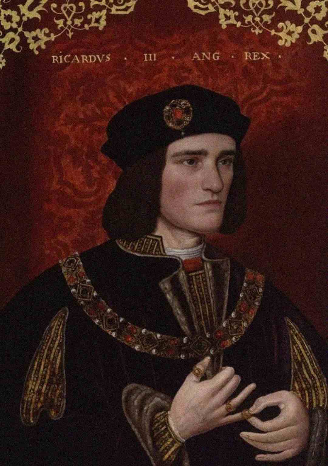 A painted portrait of a man in royal medieval clothing and a black hat, wearing ornate jewelry. The background is red with gold patterns and the words "RICARDVS III ANG REX" above his head.