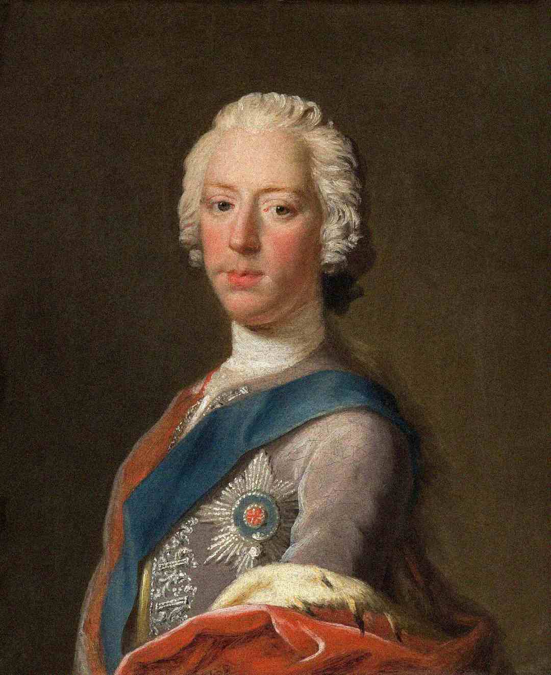 Portrait of a young man with pale skin and white powdered hair, dressed in 18th-century formal attire with a blue sash, ornate silver decorations, and a medal pinned to his chest, set against a dark background.