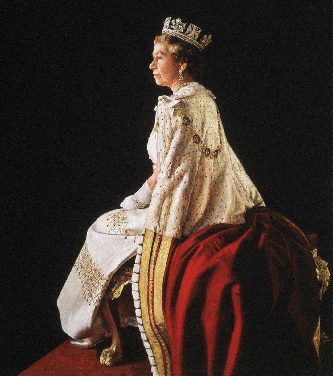 A woman wearing a crown and regal white robe with gold accents sits in profile on a golden chair draped with a red cloth, against a dark background.