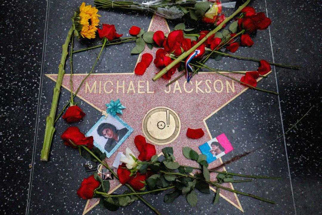 Michael Jackson’s Hollywood Walk of Fame star surrounded by red roses, a sunflower, rose petals, photos of him, and small tributes, honoring his memory.