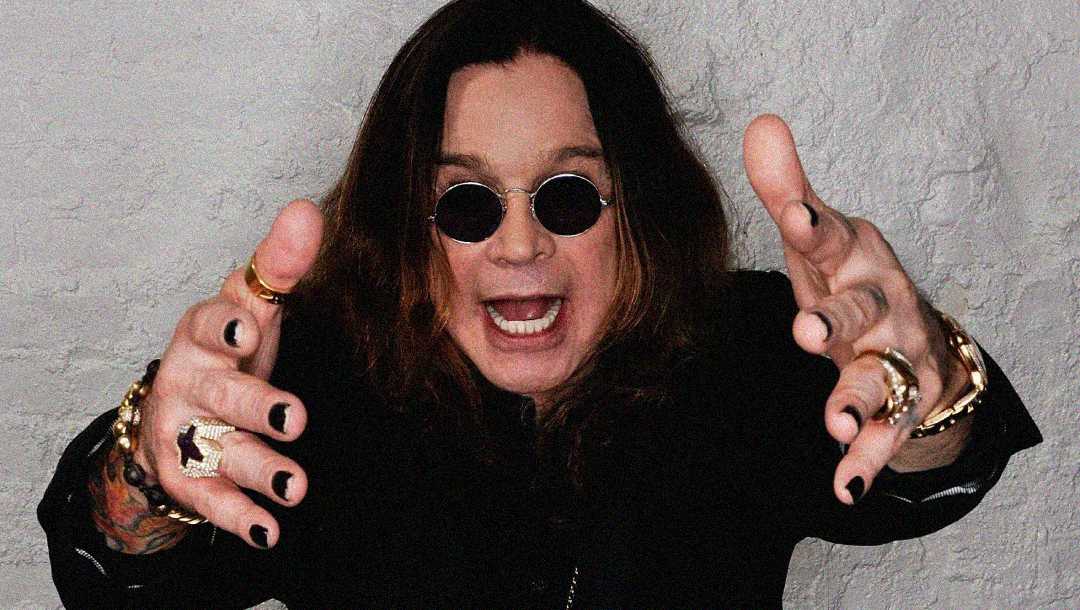 A person with long brown hair, wearing black round sunglasses and black clothing, reaches toward the camera with hands outstretched, showing black nail polish and several rings against a light textured background.