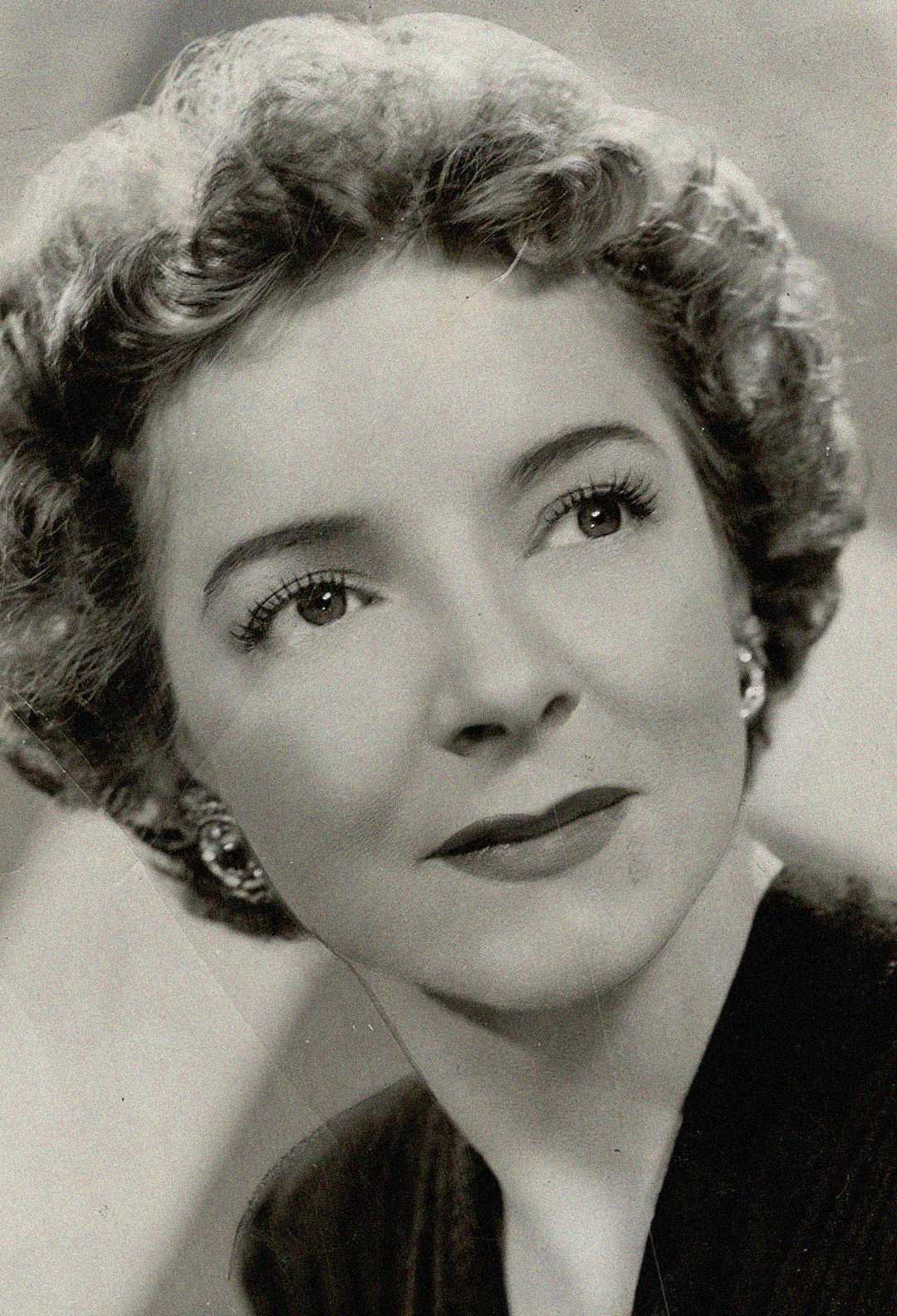 Black and white portrait of a woman with short, curly hair, wearing earrings and a dark top, looking slightly upward with a gentle expression.