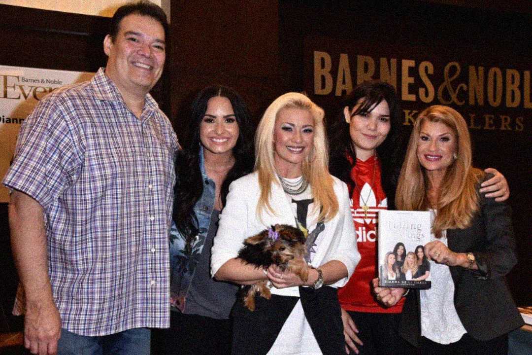 A group of five people pose and smile at a Barnes & Noble event. One woman holds a small dog, another holds up a book. They stand closely together in front of a bookstore sign.