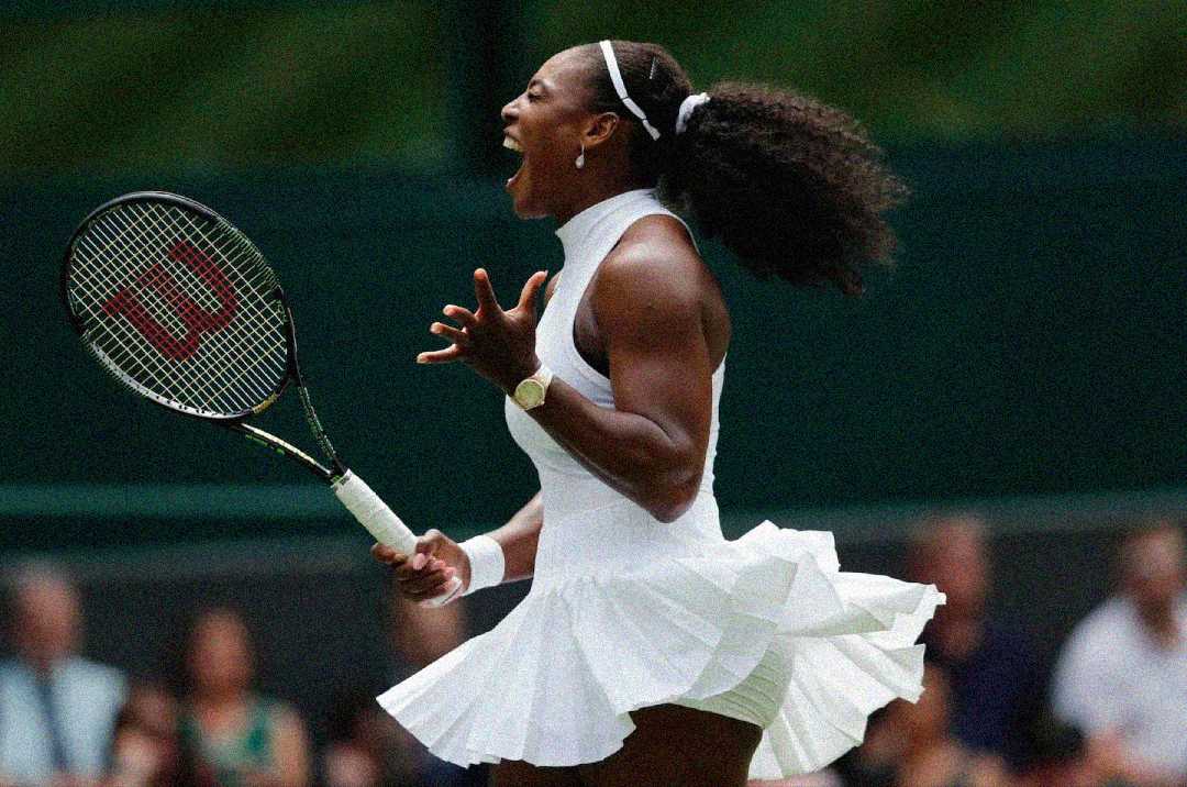 A female tennis player in a white outfit passionately celebrates on the court, holding a racquet with her mouth open in a yell, her skirt and hair in motion.
