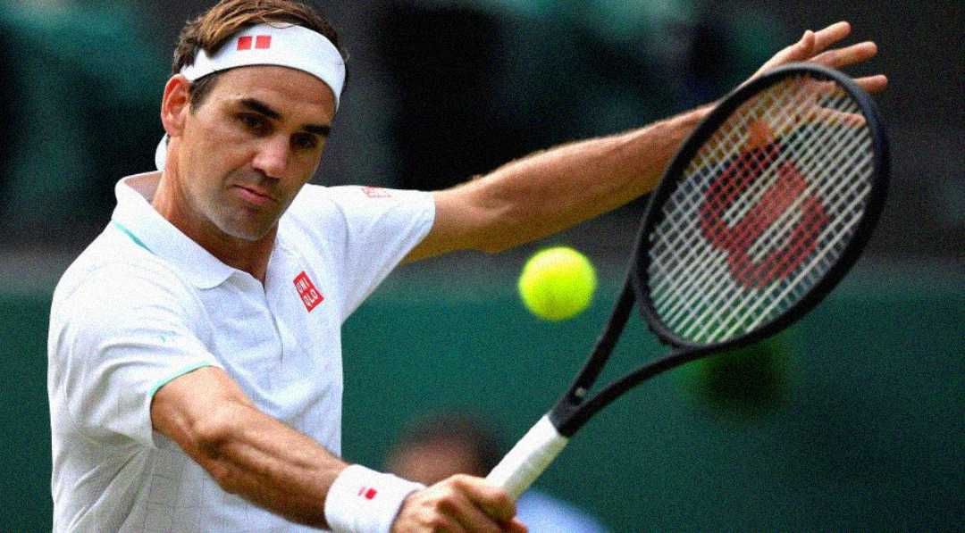 A tennis player in a white shirt and headband hits a two-handed backhand shot during a match, focusing on the yellow ball approaching his racket.