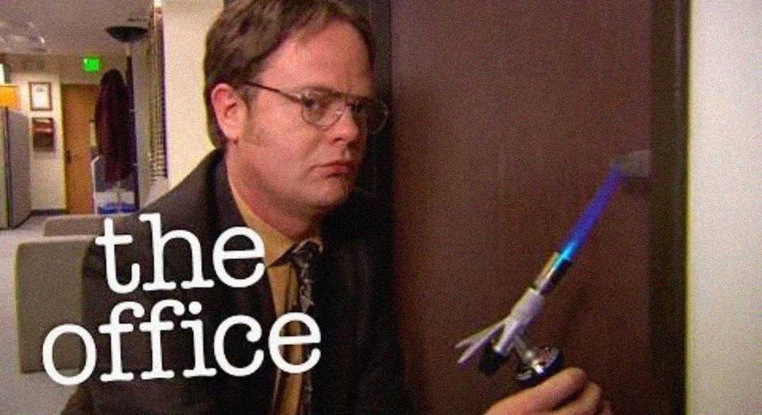 A man in glasses and a suit uses a small blowtorch on an office door. The words "the office" appear over the image.