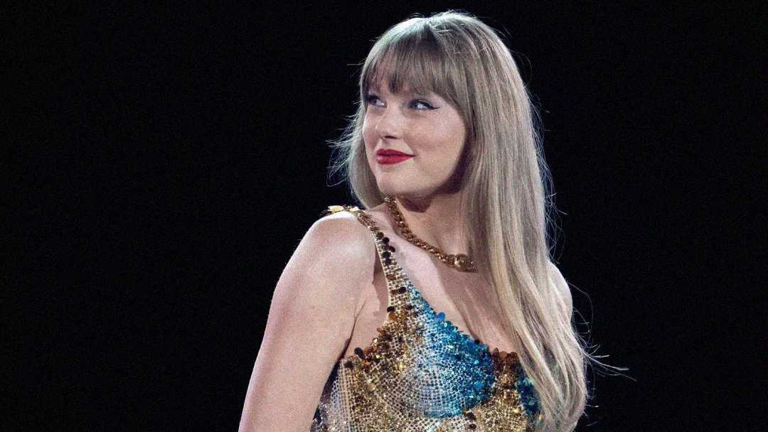A woman with long blonde hair and red lipstick wears a sparkly, multicolored sleeveless dress, looking off to the side against a dark background.