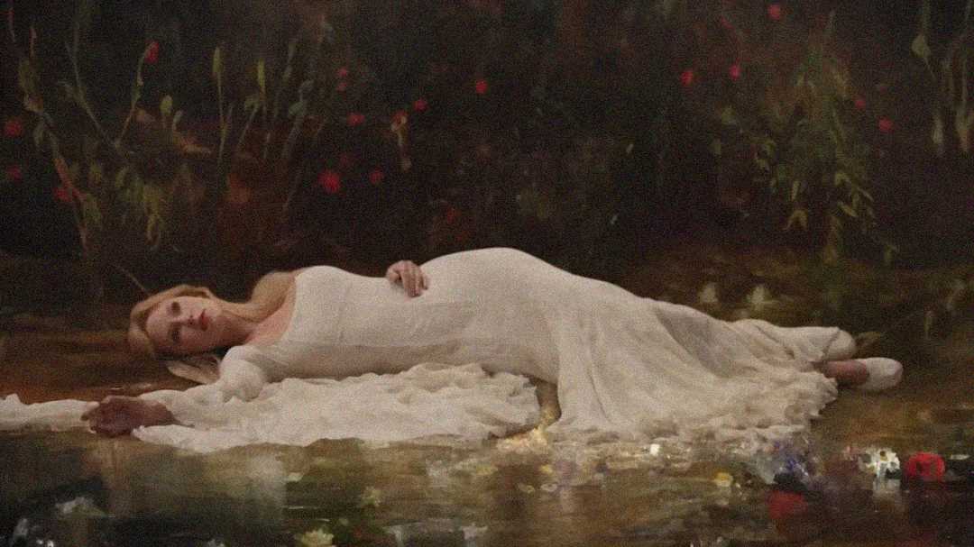 A woman in a long white dress lies on her side in a peaceful, natural setting, surrounded by greenery and flowers, with part of her gown trailing into a reflective surface, possibly water.