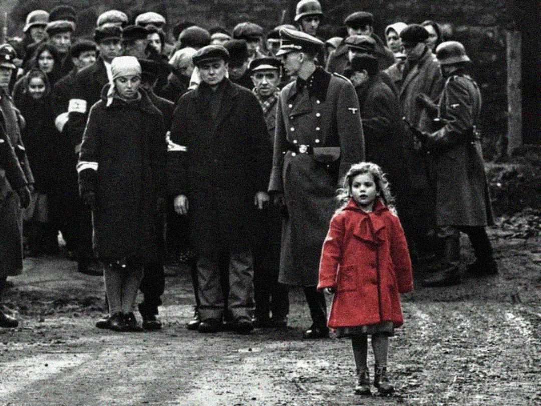 A young girl in a bright red coat stands in the foreground, while a crowd of people and Nazi soldiers in dark clothing gather in the background, creating a stark contrast. The image is mostly in black and white except for the red coat.