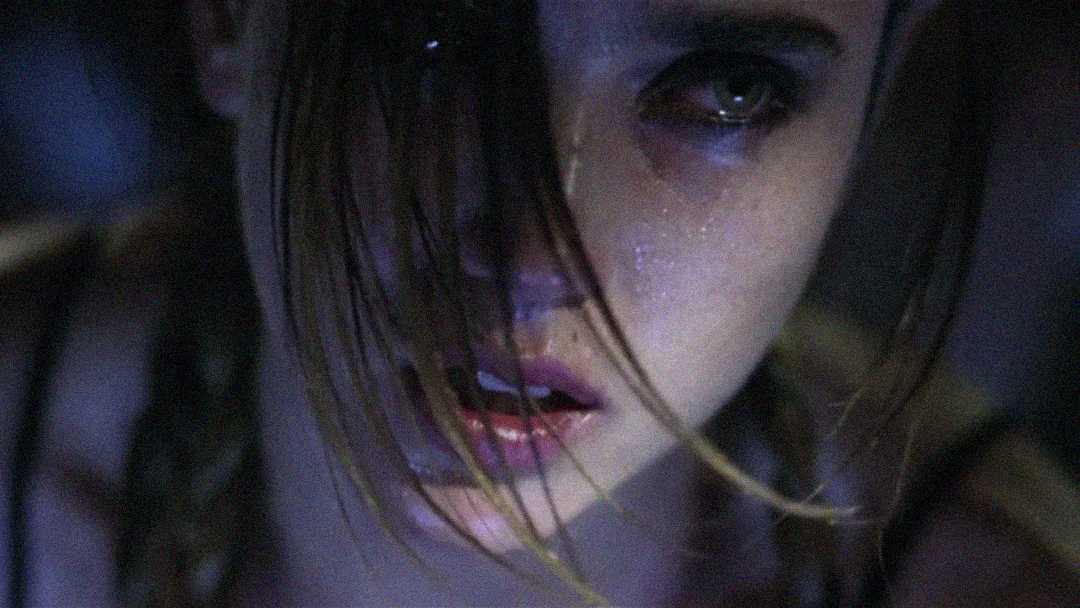 A close-up of a young person with tears on their face, looking distressed. Strands of hair partially cover their face, and the lighting is dim and dramatic, highlighting their emotional expression.
