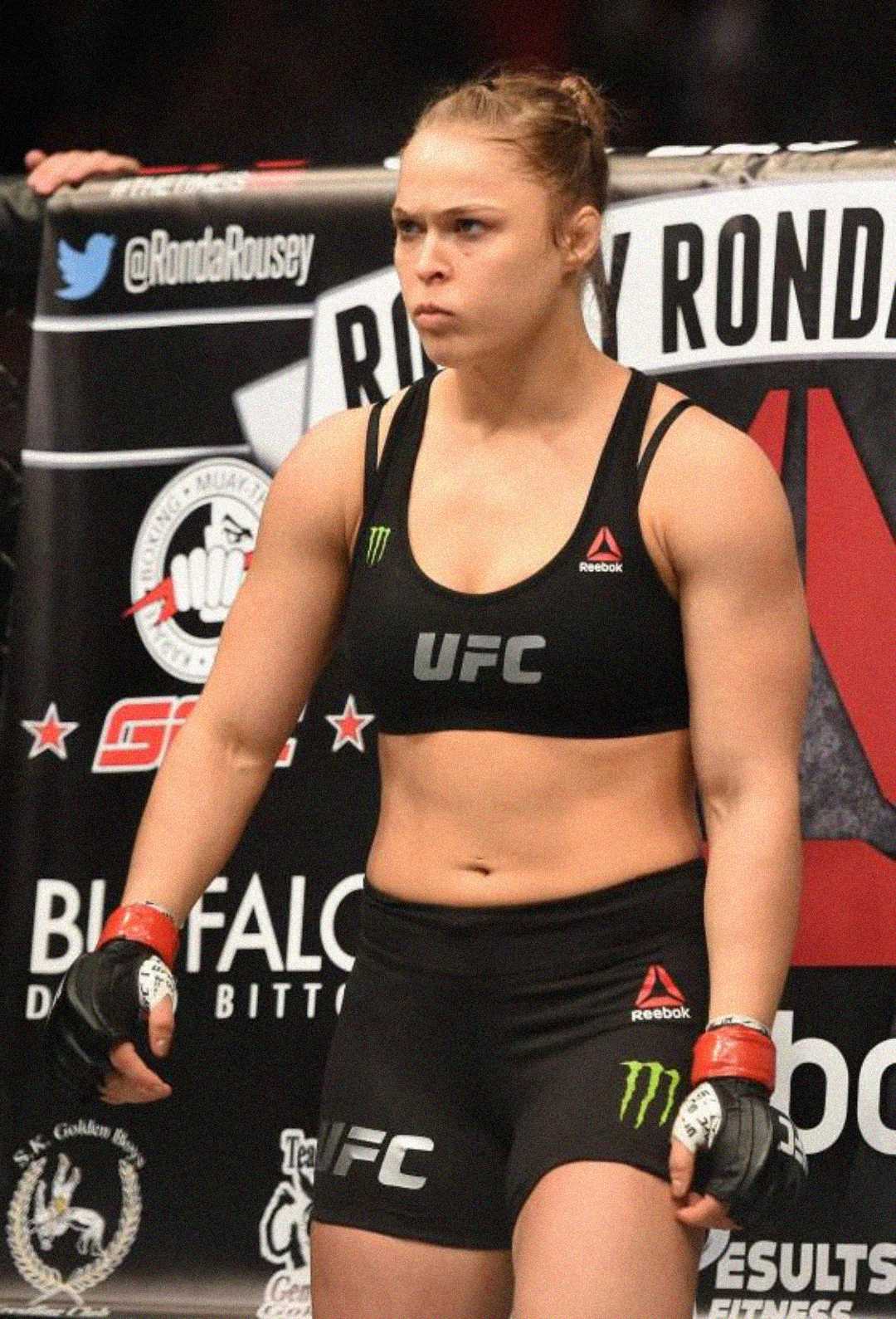 A female MMA fighter in UFC gear stands in the octagon, looking focused and intense, with her fists clenched and hair tied back, preparing for a match.
