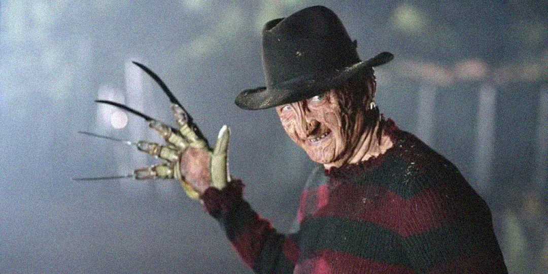 A menacing figure in a brown fedora and red-and-green striped sweater holds up a gloved hand with long, sharp blades as fingers, standing in a foggy, dimly lit setting.