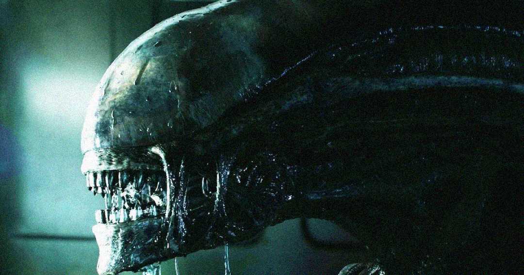 Close-up of a dark, menacing alien creature with a shiny, elongated head, sharp metallic teeth, and drool dripping from its mouth, set in a dimly lit environment.