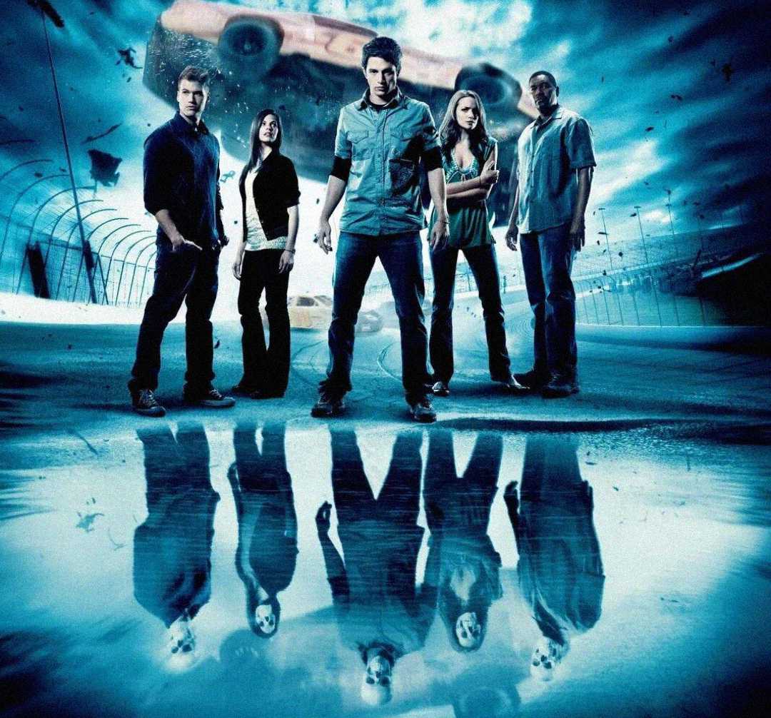 Five people stand side by side on a racetrack with intense expressions, their reflections visible below. A race car flies through the air in the background with swirling blue effects.
