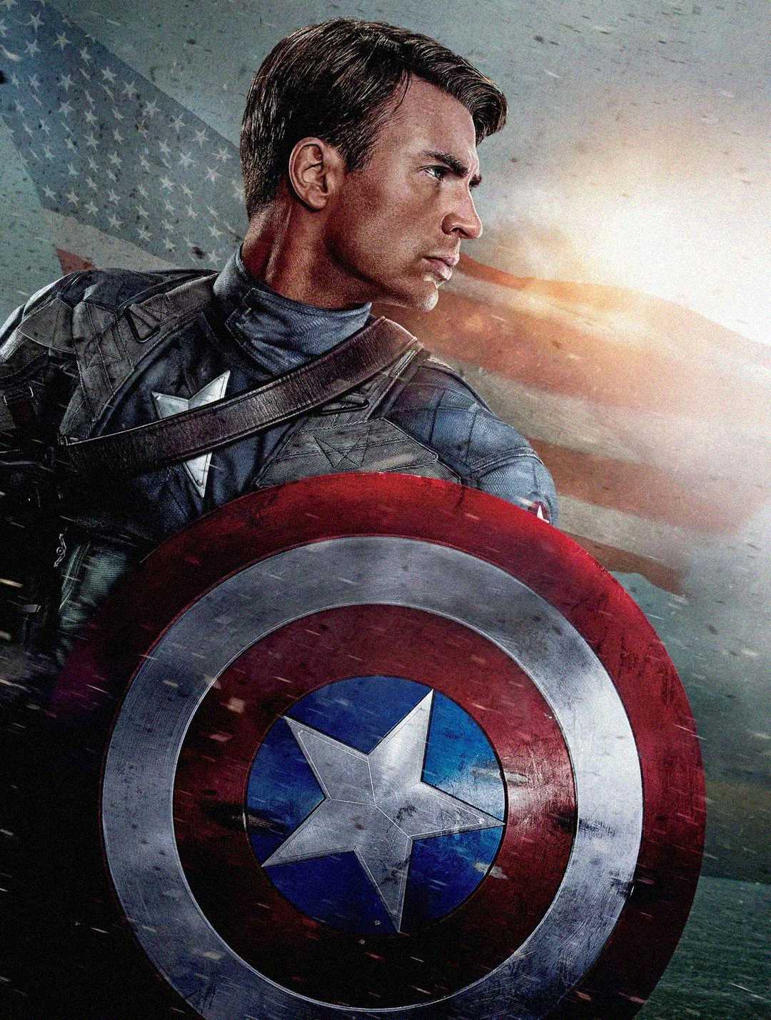 A man in a superhero costume holds a red, white, and blue shield with a star. He looks to the side with a serious expression, while an American flag waves in the background with dramatic lighting.