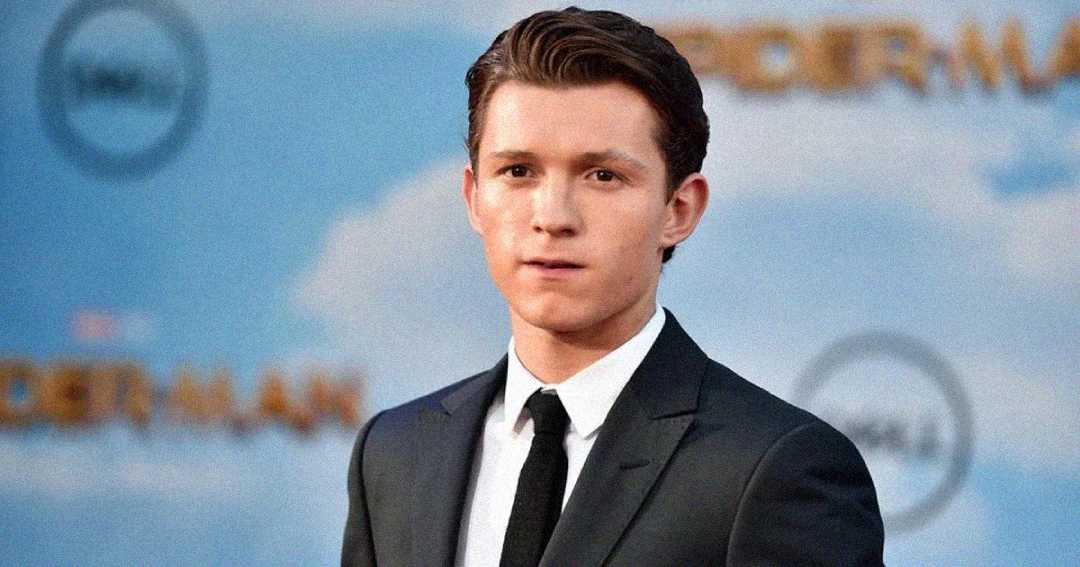 Tom Holland in a suit and tie, with a blurred "SPIDER-MAN" logo in the background.