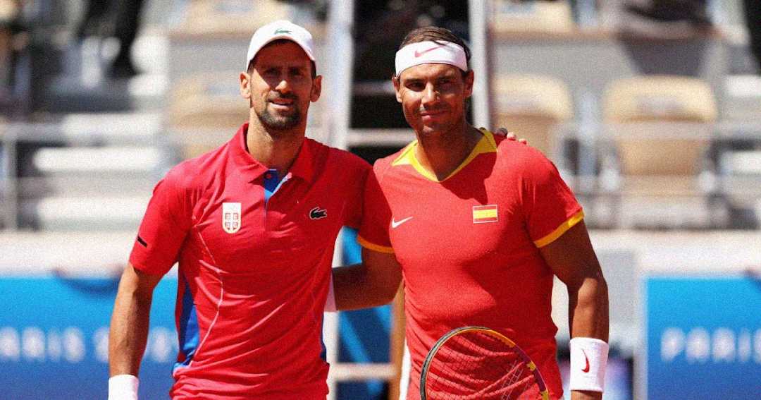 Two male tennis players in red shirts stand side by side on a tennis court, smiling at the camera, each holding a racket. They appear to represent different countries, indicated by the flags on their shirts.