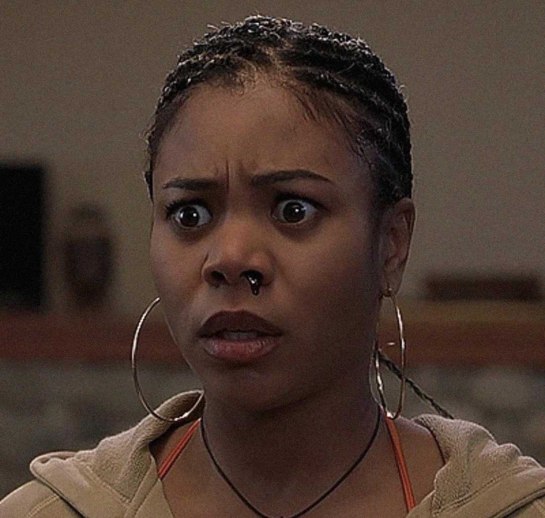 A woman with braided hair, large hoop earrings, and a nose ring looks surprised or shocked, with wide eyes and raised eyebrows.