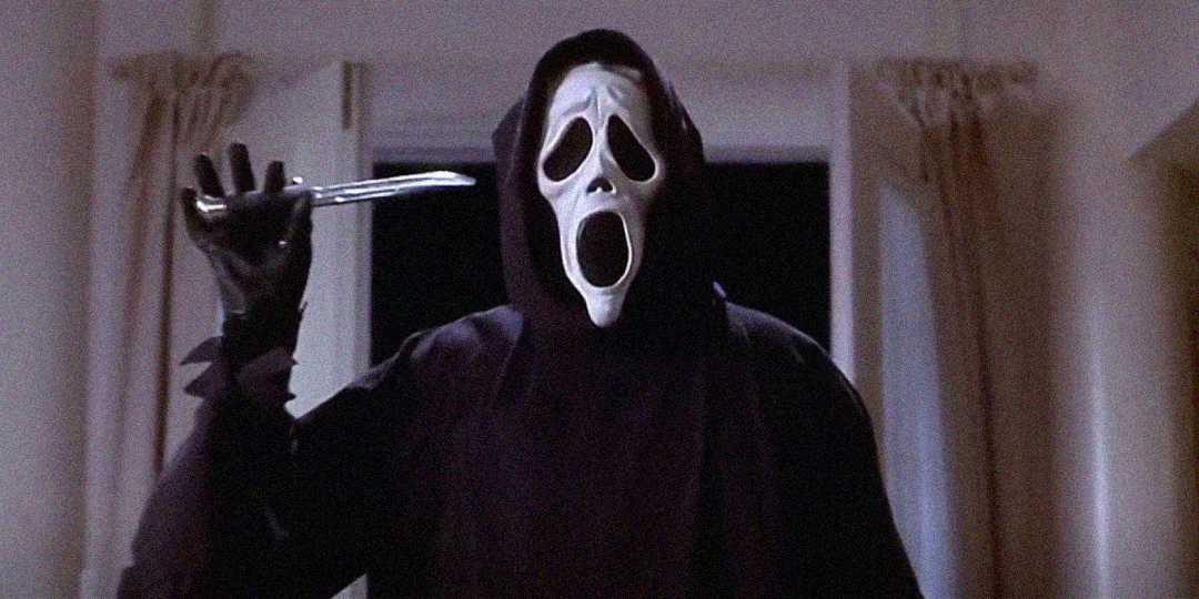 A person wearing a black hooded robe and a white, ghostly mask holds a knife raised in one hand, standing in a dimly lit room with light-colored curtains in the background.