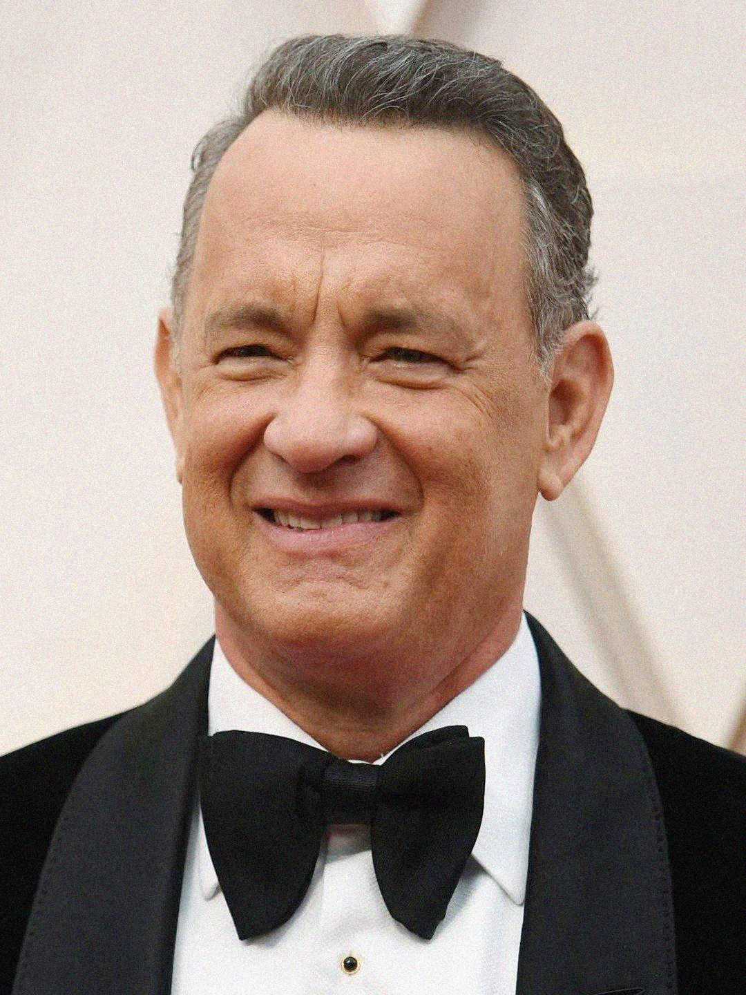 A man with short gray hair smiles while wearing a black tuxedo, white shirt, and black bow tie, posing in front of a light-colored background.