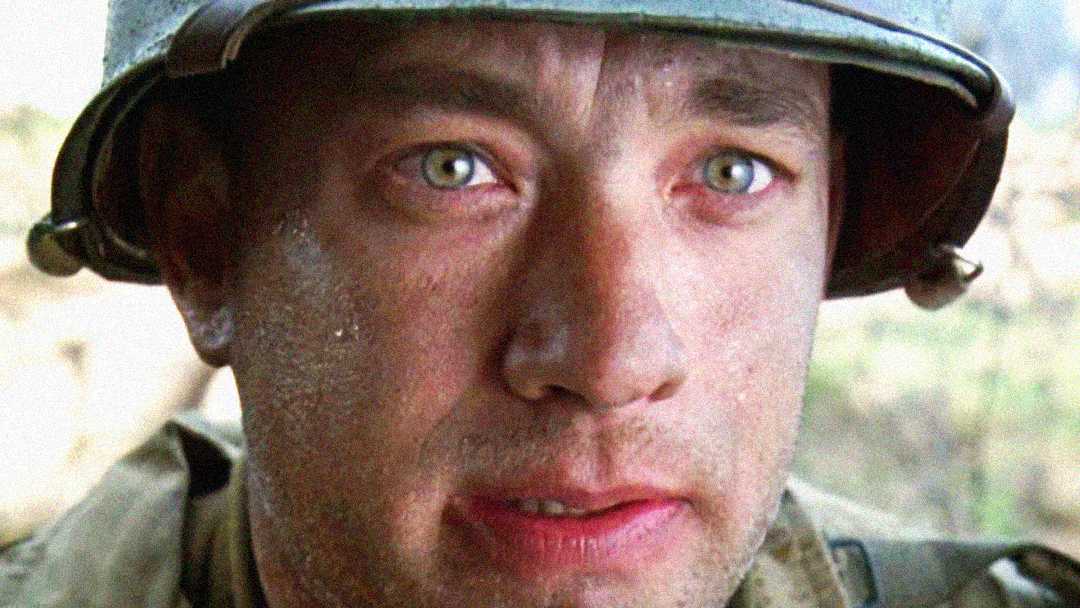 A close-up of a man in a worn military helmet and uniform, with a serious and emotional expression, his face sweaty and slightly dirty, set against a blurred outdoor background.