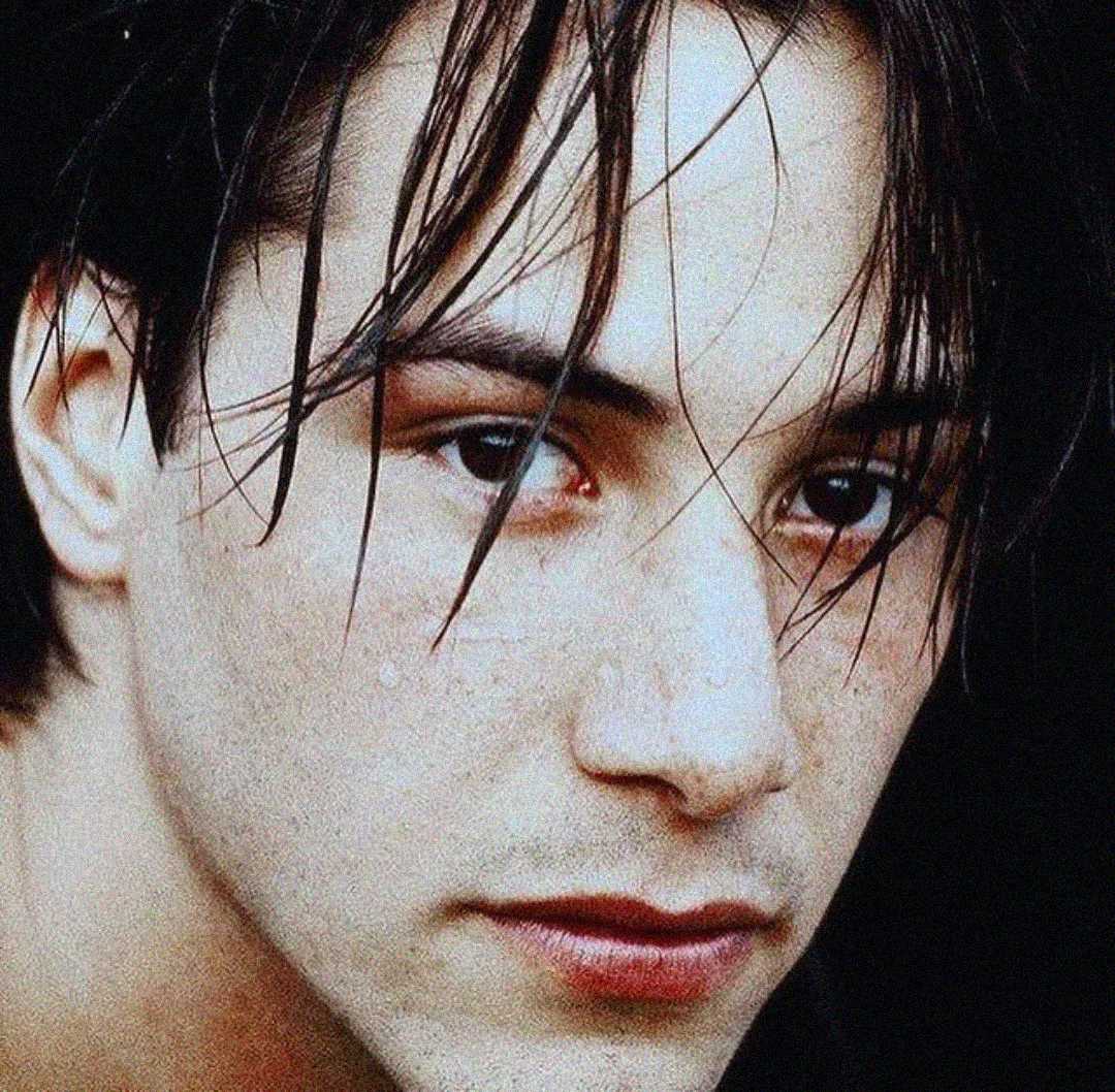 A close-up of a young person with pale skin, dark eyes, and straight brown hair partially covering their face, looking directly at the camera with a neutral expression.