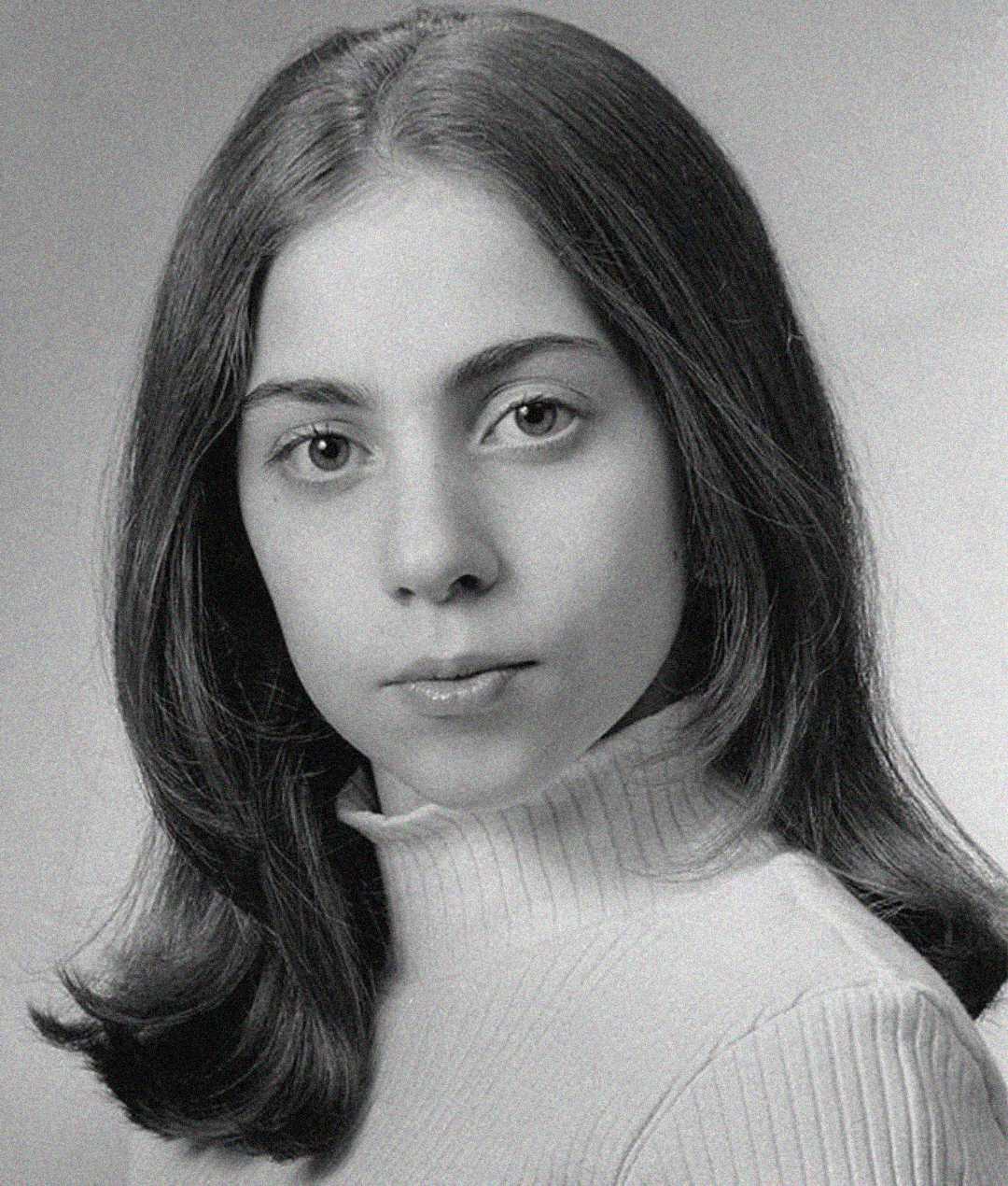Black and white portrait of a young person with straight, shoulder-length hair, wearing a light-colored turtleneck sweater, looking calmly at the camera with a neutral expression.