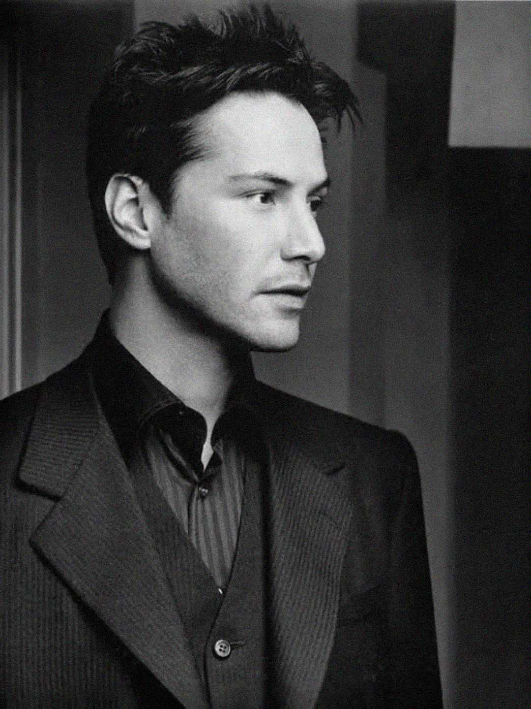 A man with short, dark hair wearing a pinstripe suit jacket and collared shirt looks to the side in a black and white portrait, set against an indoor background.