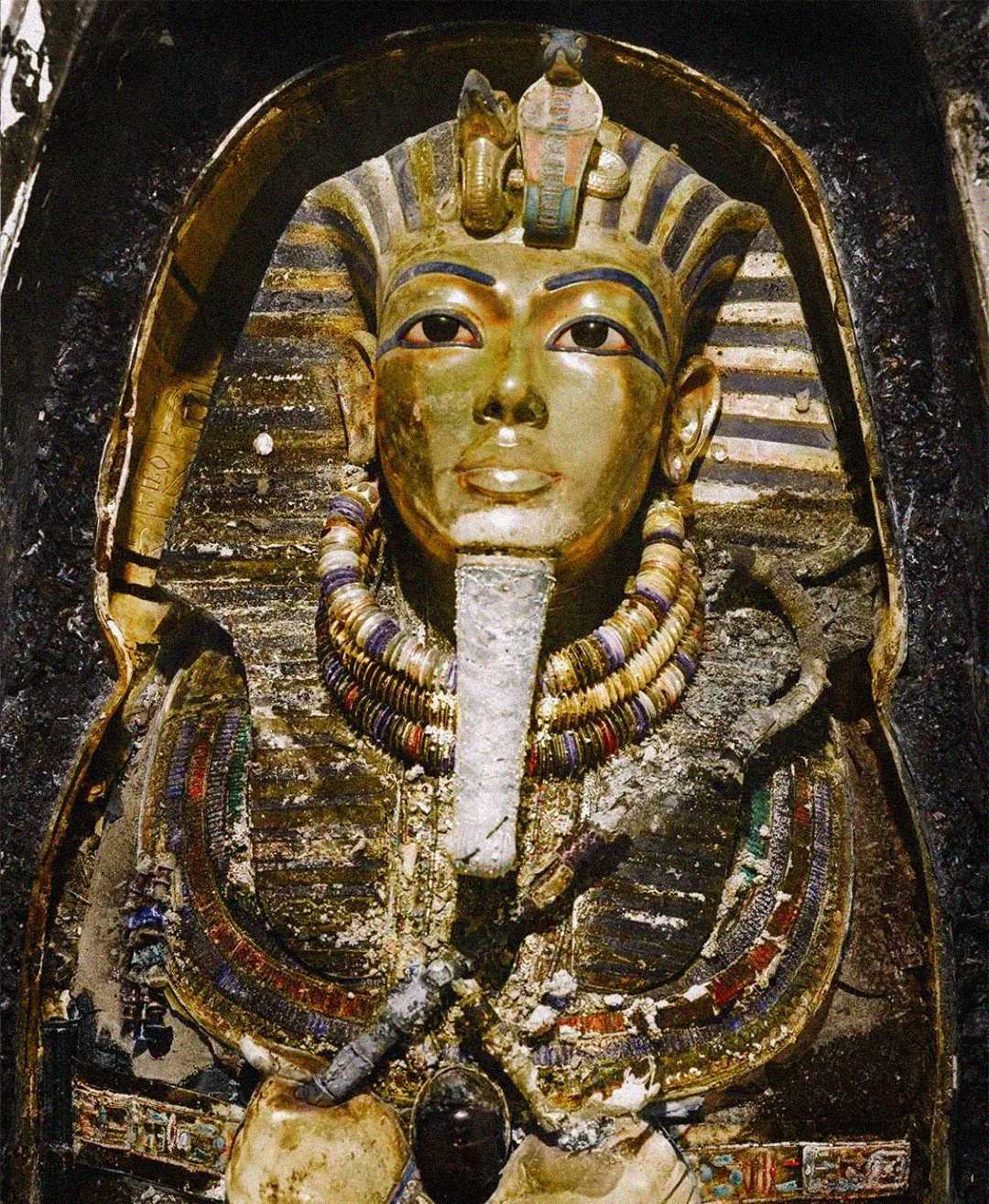 Golden mask of an ancient Egyptian pharaoh adorned with blue and gold stripes, intricate jewelry, and detailed carvings, surrounded by an ornate sarcophagus.