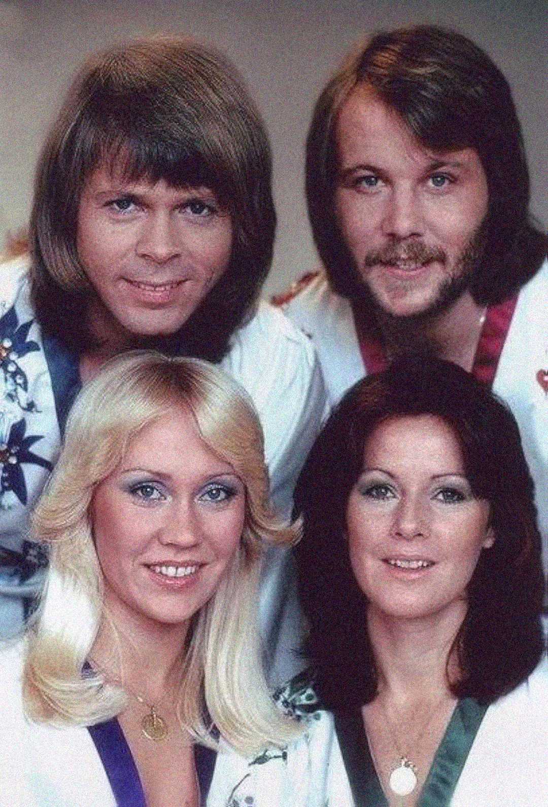 Four people posing together, two men standing behind two women. All are smiling and wearing matching light-colored outfits with patterns. The photo has a retro style and appears to be from the 1970s.
