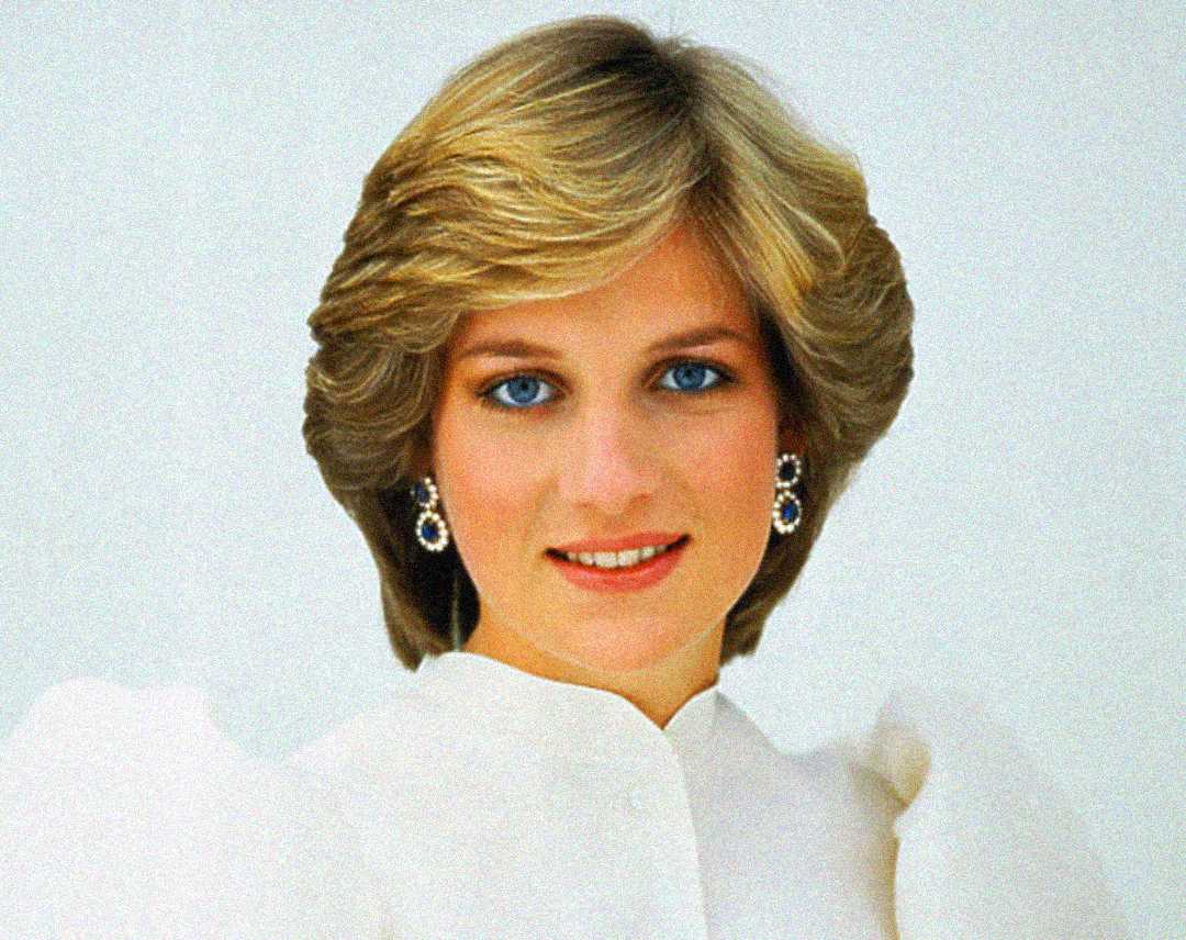 A woman with short, light-blonde hair and blue eyes smiles at the camera, wearing a white blouse and elegant blue and silver earrings against a plain light background.
