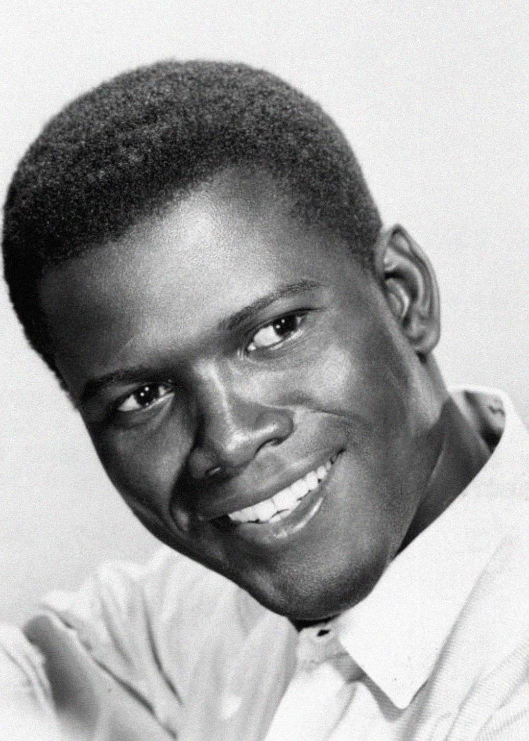 A black-and-white portrait of a smiling young man with short hair, wearing a light-colored collared shirt, looking slightly to the side.
