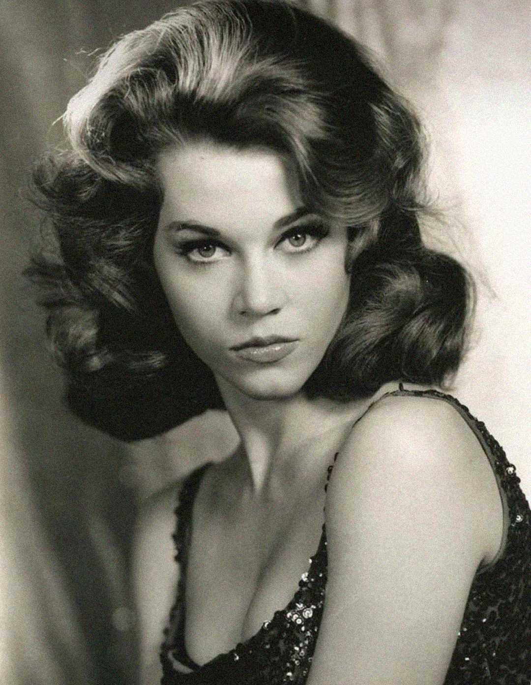 Black-and-white portrait of a woman with voluminous, wavy hair and a serious expression, wearing a sparkly, sleeveless top and looking directly at the camera.