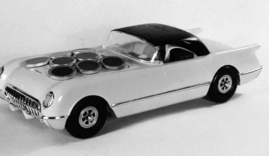 A model car with a black roof and white body, featuring six circular openings on the hood, resembling a combination of a toy car and a stove.