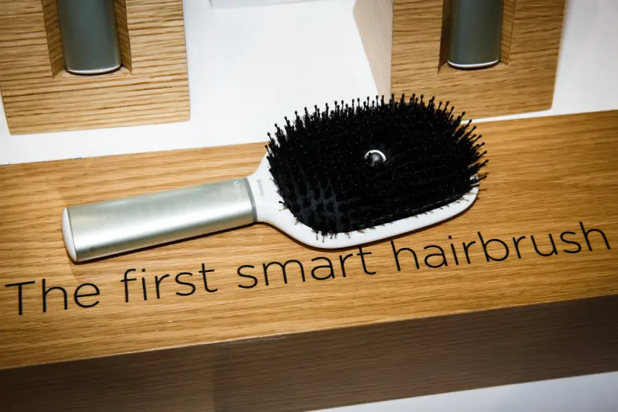 A black and silver hairbrush displayed on a wooden surface with the words "The first smart hairbrush" written below it.