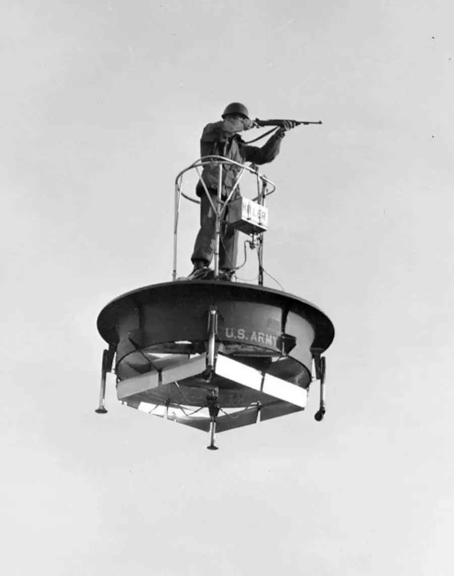 A soldier stands on a small, circular flying platform labeled "U.S. Army," aiming a rifle while elevated above the ground against a clear sky.