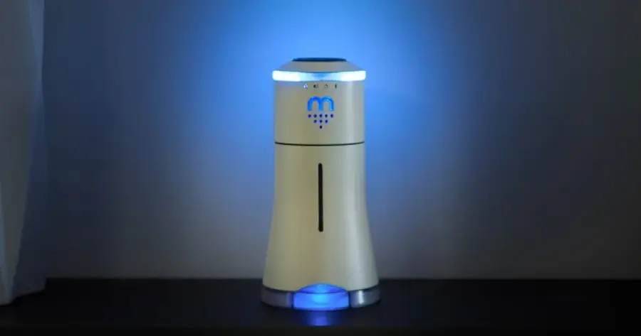 A sleek, modern air purifier with a glowing blue light stands on a dark surface against a plain wall, emitting a soft, ambient glow.