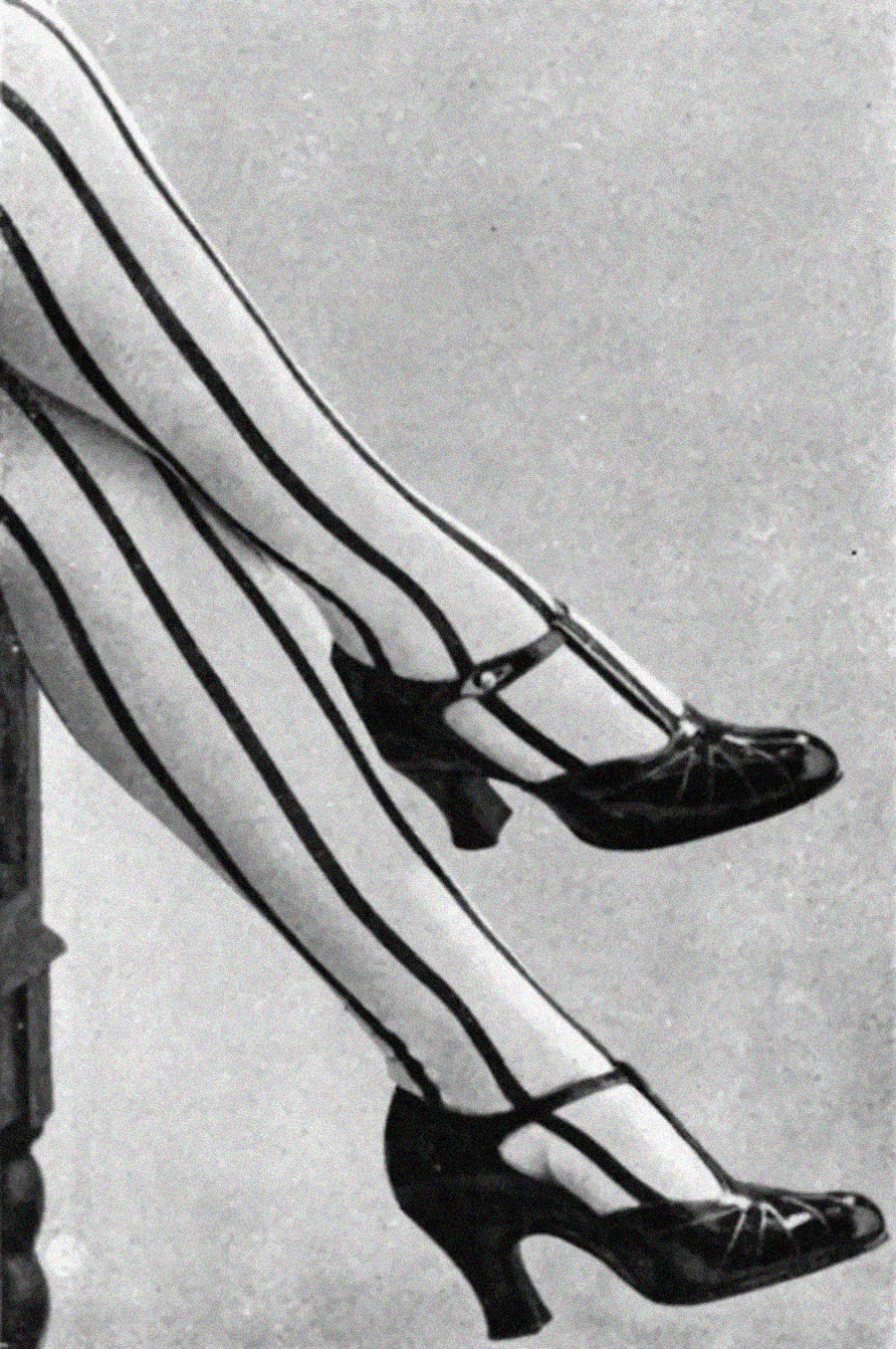 Black-and-white photo of crossed legs wearing high-heeled Mary Jane shoes and white stockings with bold vertical black stripes.