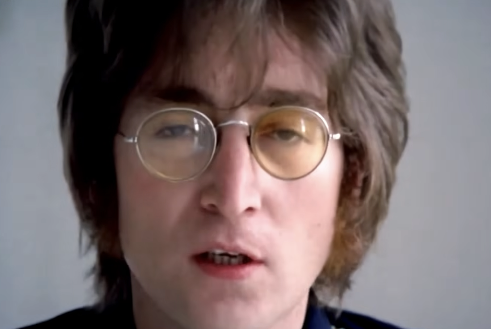 A person with medium-length brown hair, round glasses, and sideburns looks directly at the camera with a neutral expression against a plain background.