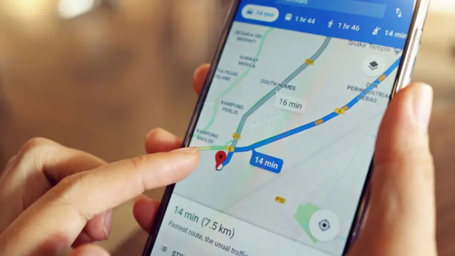 Close-up of a hand holding a smartphone with a navigation app open, showing a route on a map and an estimated travel time of 14 minutes for a 7.5 km journey.