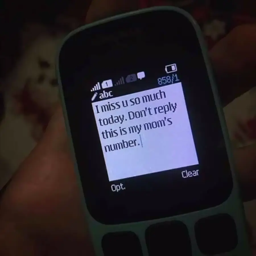 A hand holds a phone displaying a text message that reads, "I miss u so much today. Don't reply this is my mom's number.