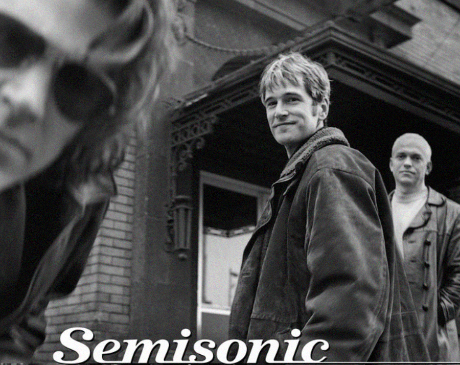 Three men in jackets stand outside a brick building, one looking at the camera, another close to the lens wearing sunglasses. The word "Semisonic" appears in large text at the bottom of the image.