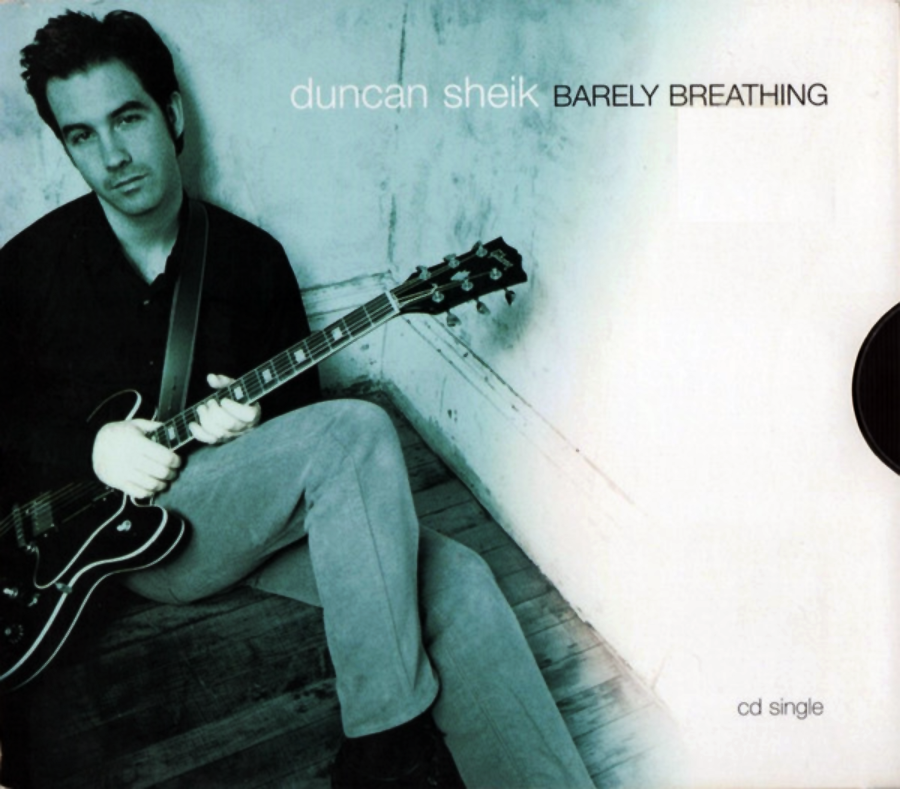 A man sits on a wooden floor in the corner of a room, holding a guitar. The text reads "duncan sheik BARELY BREATHING" and "cd single" on a white background.