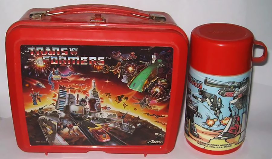 A red Transformers lunchbox with matching thermos, both featuring colorful illustrations of Transformers characters in battle amidst a futuristic cityscape.