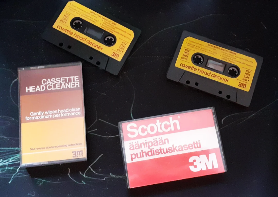 Two yellow cassette head cleaner tapes and their cases are placed on a dark surface. One case is labeled “CASSETTE HEAD CLEANER,” the other reads “Scotch äänipään puhdistuskasetti 3M.”