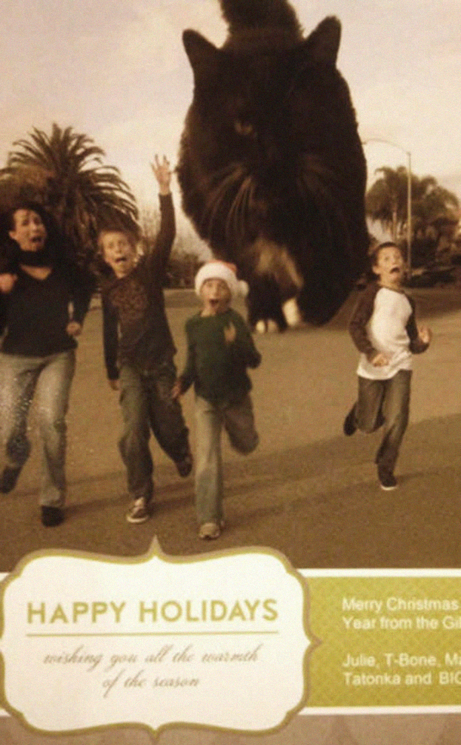 Four children run outdoors, appearing startled as an enormous black cat leaps behind them. Text at the bottom reads "Happy Holidays" with a holiday message and sender names.