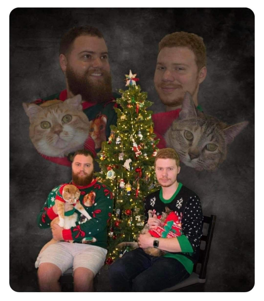 Two men in holiday sweaters sit by a decorated Christmas tree, each holding a cat. Above them are faded, floating images of their faces and their cats’ faces, all set against a dark background.