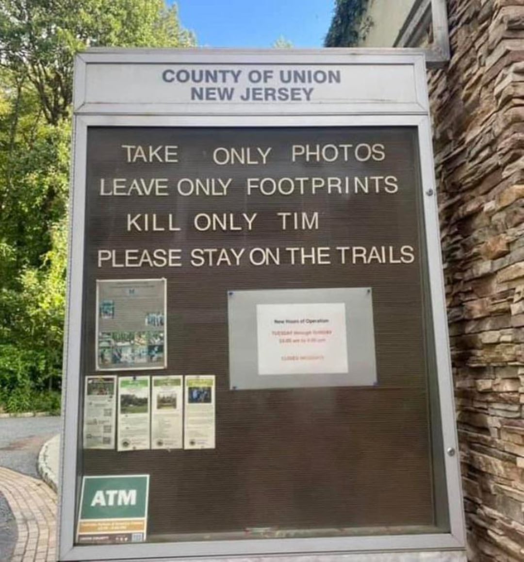 A park sign in Union County, New Jersey reads: "Take only photos, leave only footprints, kill only Tim, please stay on the trails." The phrase "kill only Tim" appears to be a humorous or mistaken addition.