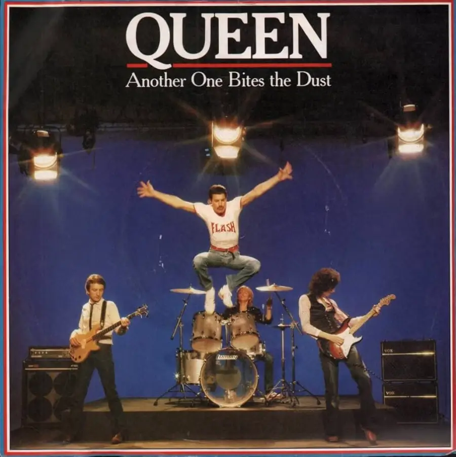 Four members of Queen perform on a stage with a blue background; Freddie Mercury is mid-air in a jump above drummer Roger Taylor, with Brian May and John Deacon playing guitar and bass on either side. Text reads, "Queen—Another One Bites the Dust.