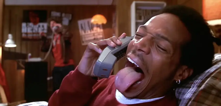 A man with his mouth wide open, showing his tongue, holding an old cordless phone to his ear.